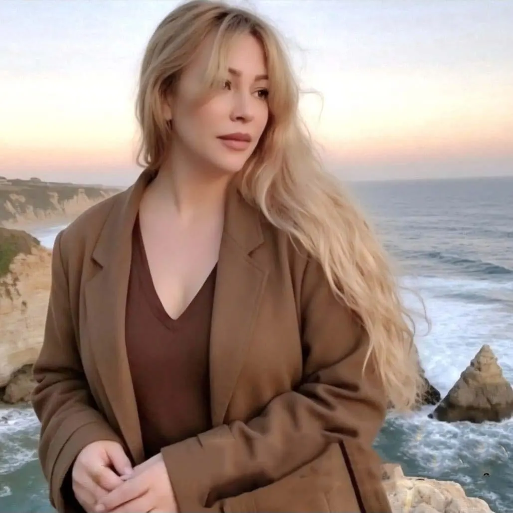 Gloria May Byron in a brown coat on a headland above the ocean at dusk